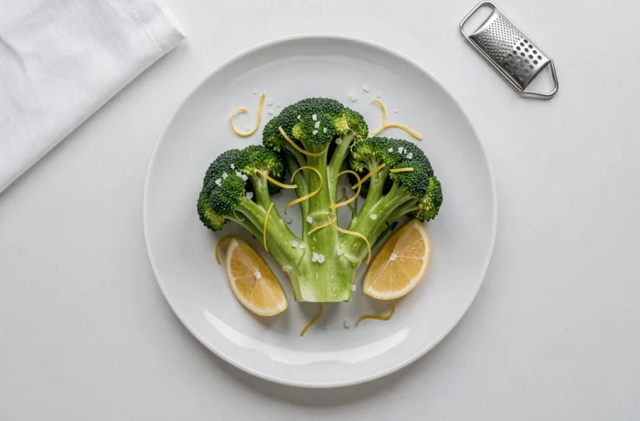 Assiette plate de brocolis vapeur vert vif avec des zestes de citron en spirale et des flocons de fleur de sel